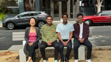 Four people sit on a bench outdoors, smiling and posing for a group photo.