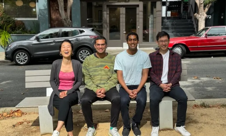 Four people sit on a bench outdoors, smiling and posing for a group photo.