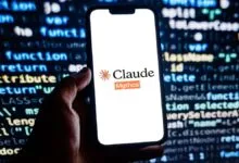 Hand holds phone displaying Claude-Mythos logo against code background.