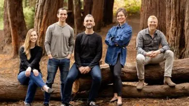 Five people pose outdoors, sitting and standing on a fallen tree trunk.