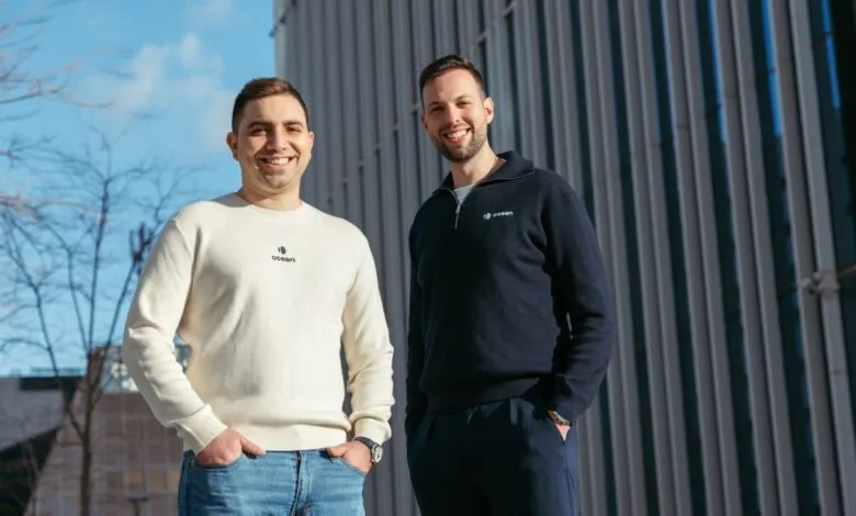 Two men smiling, wearing 'Ocean' branded sweaters, stand outdoors.