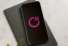 Smartphone displaying a pink logo on a black screen, resting on a dark gray notebook.