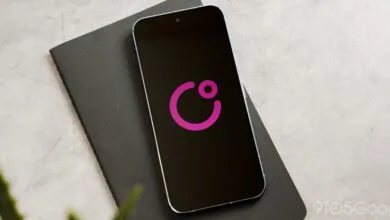 Smartphone displaying a pink logo on a black screen, resting on a dark gray notebook.