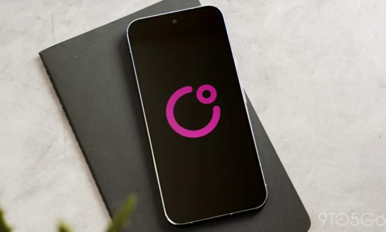 Smartphone displaying a pink logo on a black screen, resting on a dark gray notebook.