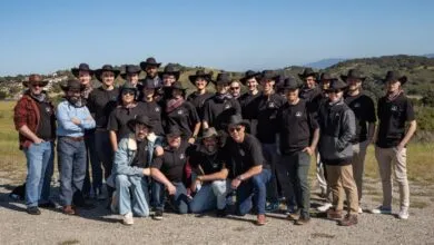 Group of about 25 people wearing cowboy hats and matching shirts posing outdoors.