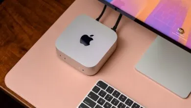 Silver Apple Mac Mini with keyboard and monitor on a pink desk mat.