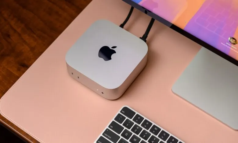 Silver Apple Mac Mini with keyboard and monitor on a pink desk mat.