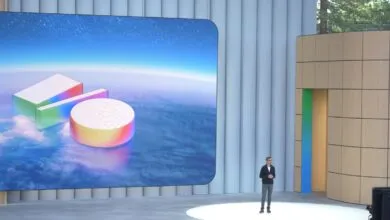 Sundar Pichai presents on stage with colorful geometric shapes on screen.