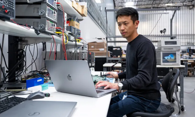 Engineer working on circuit board with laptop in a lab setting.