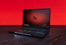 Sleek black laptop with RGB keyboard on dark wood surface.
