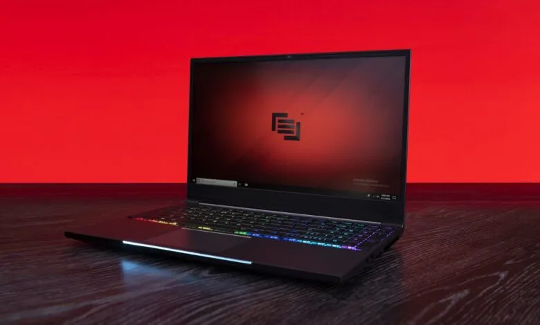 Sleek black laptop with RGB keyboard on dark wood surface.