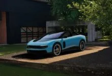 Light blue Ferrari sports car parked on concrete pad in front of modern house.