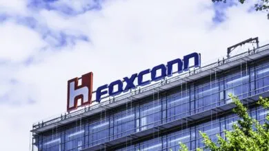 Foxconn logo on top of a modern glass building against a cloudy sky.