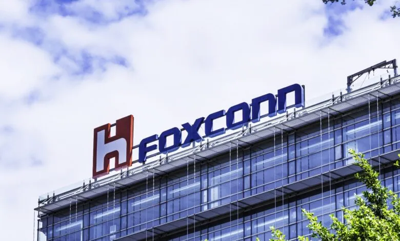 Foxconn logo on top of a modern glass building against a cloudy sky.