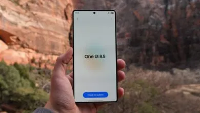 Hand holding phone displaying 'One UI 8.5' with mountain backdrop.