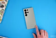 Samsung Galaxy S23 Ultra on blue background with hand touching the screen.