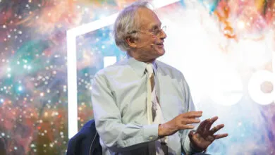Richard Dawkins speaks on stage with a colorful, cosmic background.