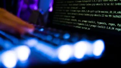 Close-up of hands typing code on a laptop with a dark screen and blue keyboard lights.