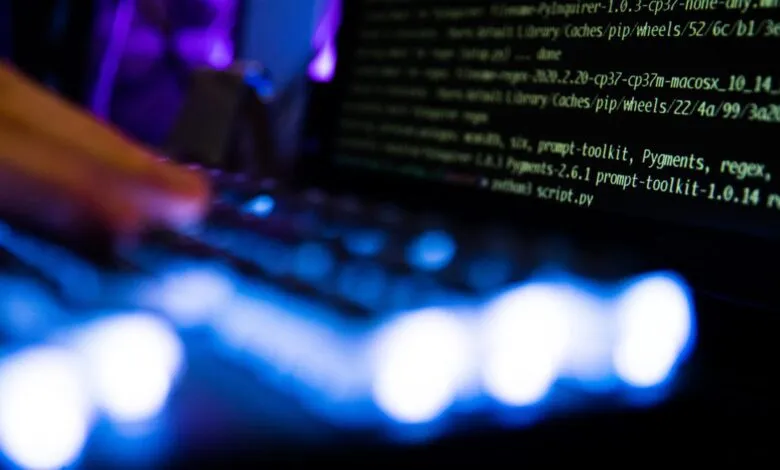 Close-up of hands typing code on a laptop with a dark screen and blue keyboard lights.
