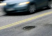 Car speeds past pothole on road with double yellow lines.