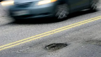 Car speeds past pothole on road with double yellow lines.