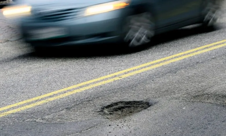 Car speeds past pothole on road with double yellow lines.