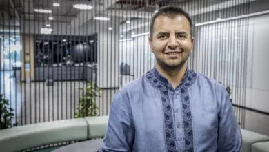 Smiling man in blue embroidered shirt stands in modern office space.