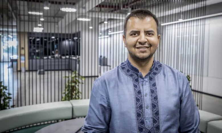 Smiling man in blue embroidered shirt stands in modern office space.