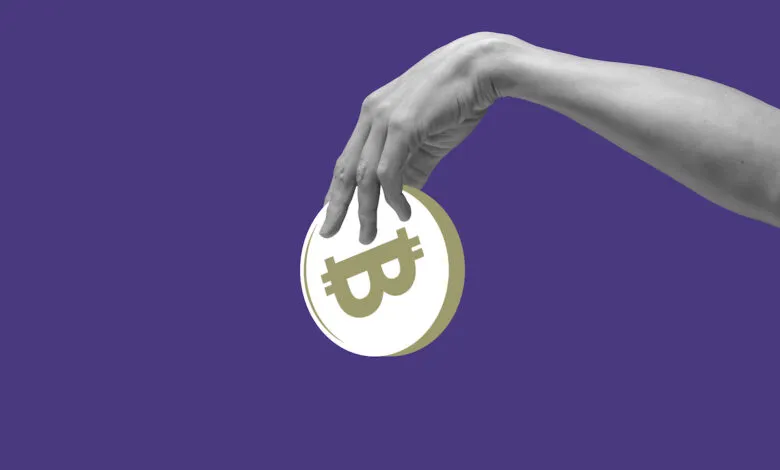 Hand holding a Bitcoin against a solid purple background.