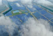 Aerial view of a large solar panel farm with wind turbines and fish ponds.