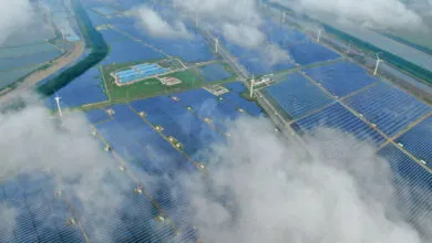 Aerial view of a large solar panel farm with wind turbines and fish ponds.