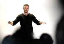Andrej Karpathy presents at a conference, gesturing with hands.