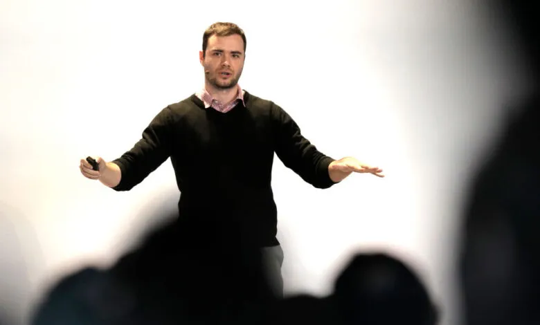 Andrej Karpathy presents at a conference, gesturing with hands.