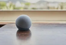 Round blue smart speaker on a polished wooden table near a bright window.