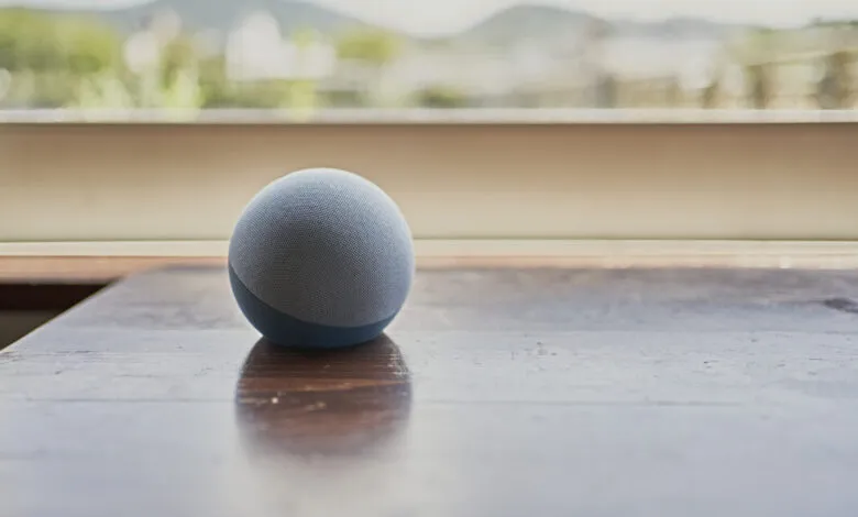 Round blue smart speaker on a polished wooden table near a bright window.
