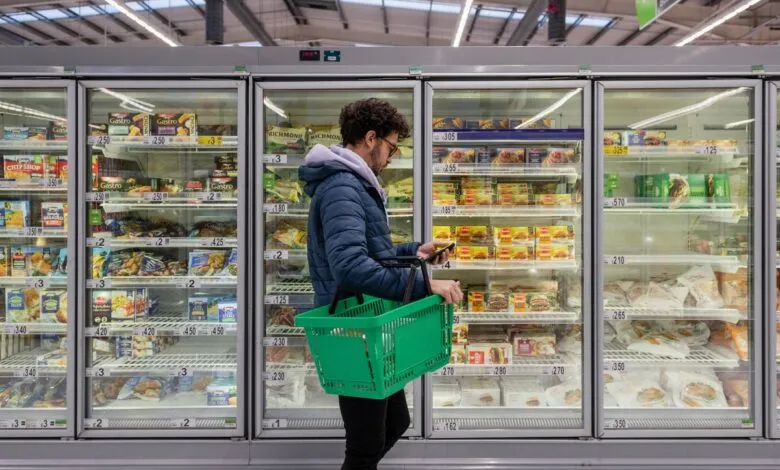 Person with green basket shops frozen foods, using phone.