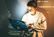 Woman in glasses codes on laptop with code projected on her face.