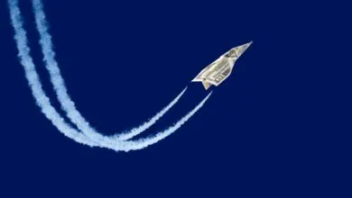 Dollar bill paper airplane soars against a deep blue sky.