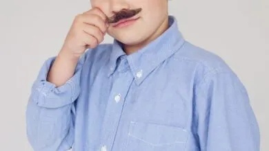 Young boy wearing a fake mustache and a blue button-down shirt.