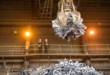 Two workers oversee a crane lifting scrap metal in a factory.