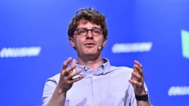 Man with glasses gestures during a presentation on stage.