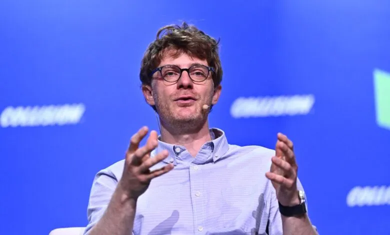 Man with glasses gestures during a presentation on stage.