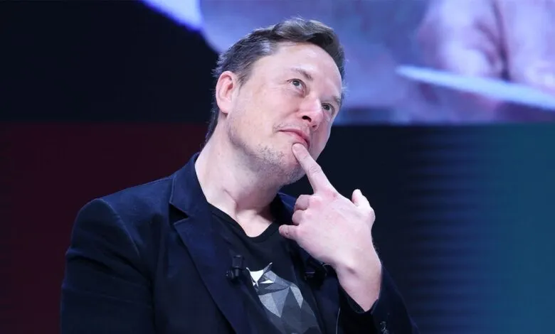 Elon Musk thoughtfully poses with finger on chin.