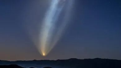 Rocket launch creates bright plume in night sky above dark mountains.