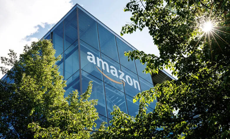 Amazon logo on modern glass building framed by green trees.