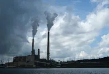 Coal-fired power plant with smokestacks emitting plumes against a cloudy sky.