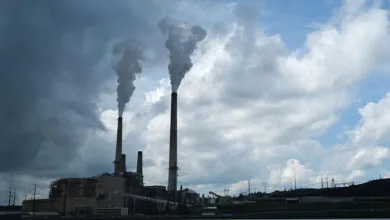 Coal-fired power plant with smokestacks emitting plumes against a cloudy sky.