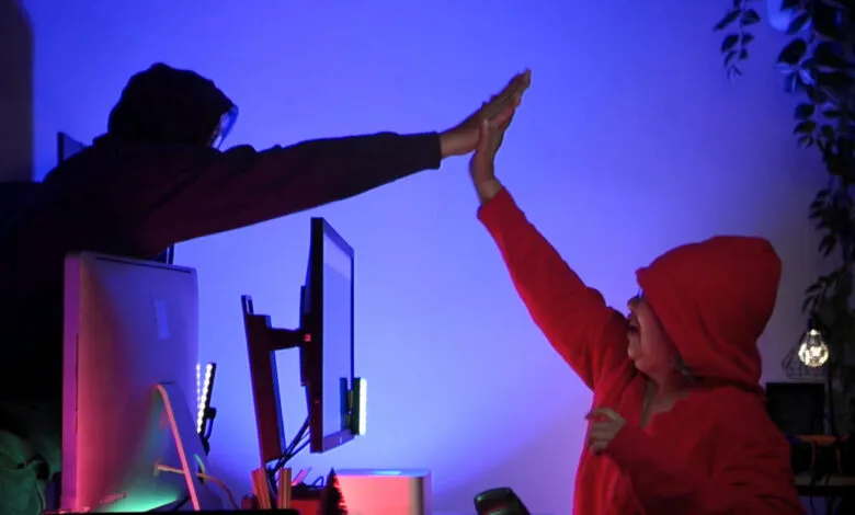 Two people in hoodies high-fiving in front of computer screens.