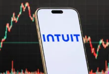 Smartphone displays Intuit logo against stock market chart background.