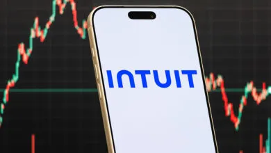 Smartphone displays Intuit logo against stock market chart background.